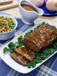 meatloaf with gravy, carrots and peas on a plate next to two bowls of vegetables