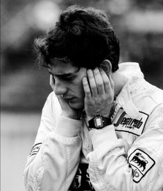 a black and white photo of a man holding his hands to his face while wearing a racing suit