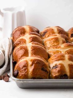 freshly baked hot cross buns in a baking pan with chocolate chips on the side