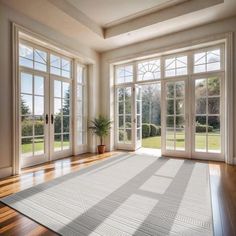 an empty room with wooden floors and large windows on both sides, looking out onto the yard