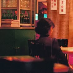 a woman sitting at a table in front of a bar with lots of bottles on it