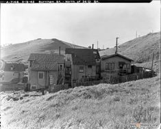 black and white photograph of an old house on a hill with mountains in the background