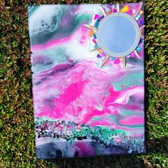 a painting is laying on the grass with a mirror in it's center,