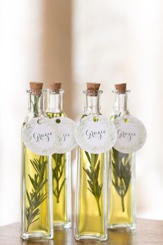 three small bottles filled with olive oil and rosemary sprigs sitting on a table