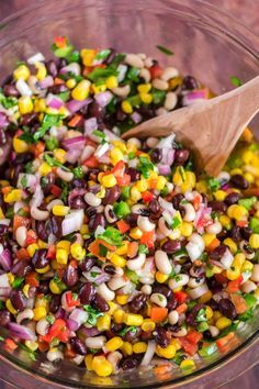 a glass bowl filled with black beans, corn and cilantros next to a wooden spoon