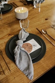 a place setting with napkins, silverware and candles on a wooden dining table