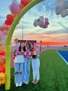 two girls holding up a sign under an arch with balloons in the background that says seniors class of 2013