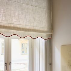 an open window with white curtains and red trim on the top, next to a bed