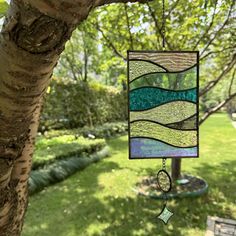 a stained glass wind catcher hanging from a tree in a yard with grass and trees