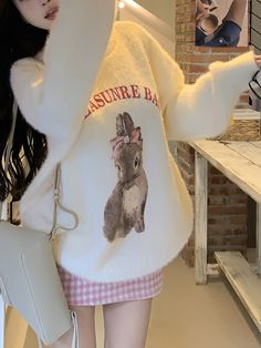 a woman wearing a white sweater with an image of a bunny on it and holding a purse