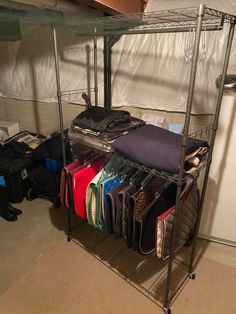 a rack filled with lots of clothes next to a white wall in a room full of bags and suitcases