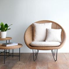 a wicker chair sitting next to two tables with pillows on them and a potted plant in the corner