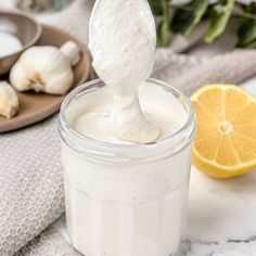 a small jar filled with mayonnaise next to sliced lemon and garlic on a table