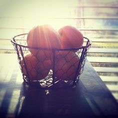 two oranges in a wire basket sitting on a wooden table next to a window