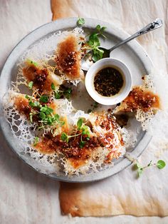 a white plate topped with food next to a small bowl of dipping sauce on top of it