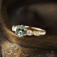 a green and white diamond ring sitting on top of a wooden table next to a vase