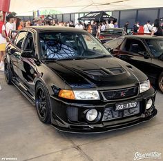 two black cars parked next to each other in front of a crowd at a car show