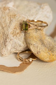 two gold rings sitting on top of a rock next to a piece of stone with a green tourmaline in it