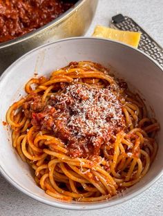 a white bowl filled with spaghetti and sauce next to a pan of cheese covered pasta