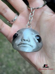 a hand holding a metal keychain with a face on it