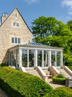 a stone house with white windows and steps leading up to the front door, surrounded by hedges