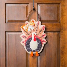 a turkey shaped door hanger hanging on a wooden door with an orange ribbon around it's neck