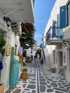 an alley way with white buildings and blue balconies on either side, surrounded by potted plants