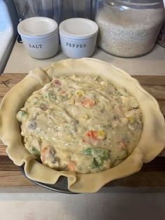 an uncooked pie sitting on top of a wooden cutting board next to containers