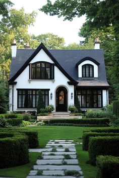 a white house with black trim and lots of windows in the front yard is surrounded by hedges