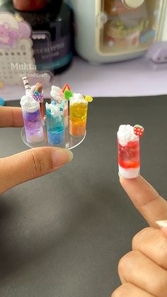 someone is pointing at miniature cocktails on a fingernail holder that they are holding