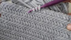 someone is crocheting the edges of a gray blanket with a purple handled knitting needle