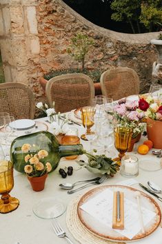 the table is set with flowers, plates and utensils for an outdoor dinner