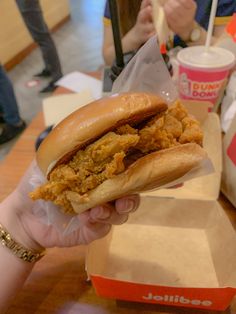 a person holding a sandwich in their hand at a fast food restaurant with two drinks