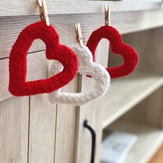 two crocheted hearts hanging from clothes pins on a hook in front of a book shelf