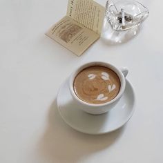 a cappuccino on a saucer next to an open book