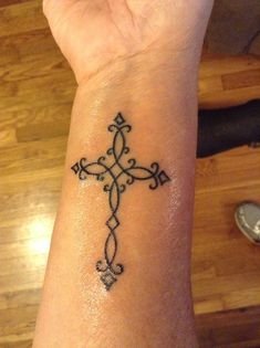 a cross tattoo on the wrist is shown in black ink, and it appears to be an intricate design