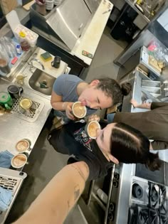 two men are in the kitchen drinking from cups with their faces close to each other