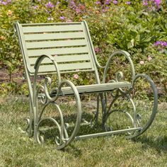 a metal chair sitting on top of a green grass covered park bench next to flowers