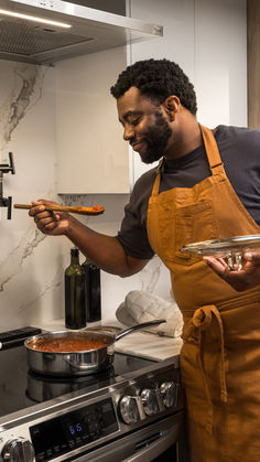 a man in an orange apron is holding a pan with food on it while standing next to the stove