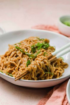 a white plate topped with noodles and chopsticks on top of a pink table cloth