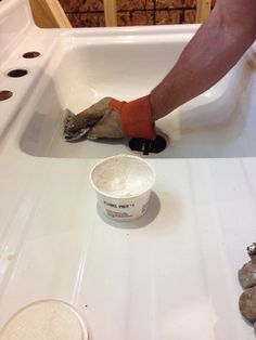 a person in orange gloves is painting a white sink