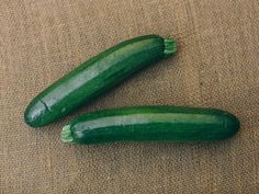 two green cucumbers sitting next to each other on a brown tablecloth covered surface