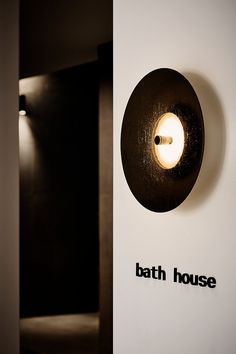 a bathroom sign with the word bath house on it's side and an illuminated light in the middle