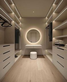 an empty walk in closet with white drawers and lights on the ceiling, along with a round mirror