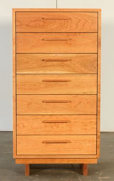 a wooden chest of drawers sitting on top of a cement floor next to a white wall