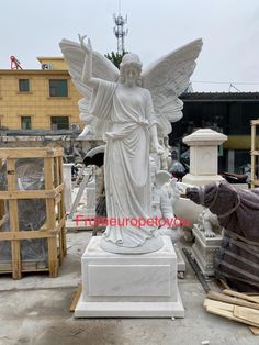 an angel statue sitting on top of a white marble pedestal next to other statues in front of a building