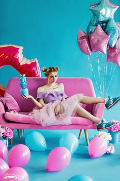 a woman sitting on a pink couch surrounded by balloons