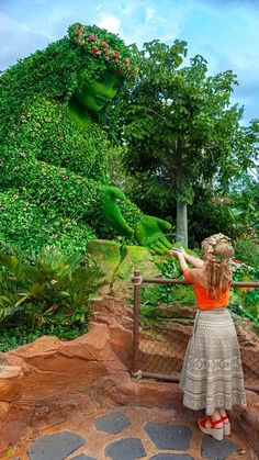 a woman standing on top of a bridge next to a lush green tree covered hillside