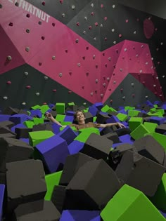 a woman is in the middle of an indoor climbing wall with colored blocks on it