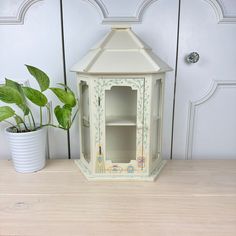 a potted plant sitting next to a white wooden shelf with a painted birdhouse on it